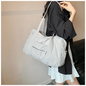 Detail of light grey nylon shoulder bag featuring metal zipper pocket and embroidered logo