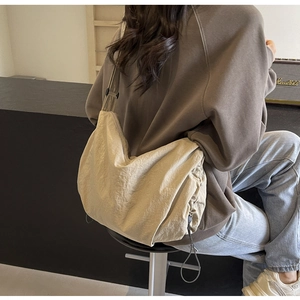 Adjustable wide strap and side drawstring detail on a beige textured crossbody bag