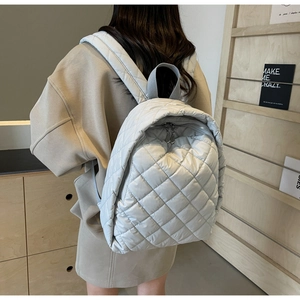 Seitenansicht eines gesteppten silbernen Rucksacks, getragen von einem Model im Regal