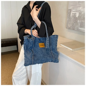 Detail of blue denim tote bag with brown leather patch and embossed Penny logo branding