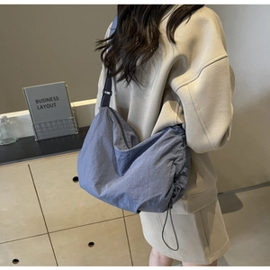 Detail of navy blue nylon crossbody bag featuring adjustable straps and drawstring side
