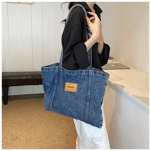 Detail view of large denim canvas tote bag with a brown leather penny patch and shoulder strap