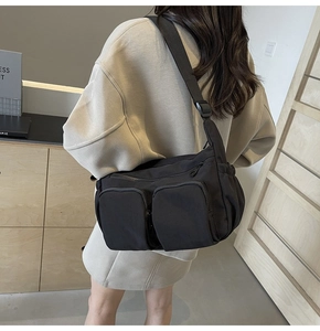 Detail view of black nylon crossbody bag with multiple functional zipper pockets and wide strap