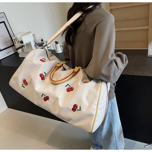 Close-up of cream canvas tote featuring red cherry embroidery and yellow leather trim