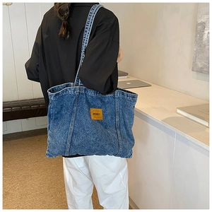 Lifestyle shot of large denim tote bag with Penny leather patch on a model's shoulder