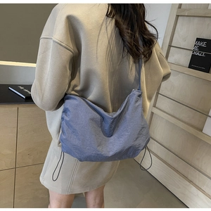 Detail of blue textured nylon crossbody bag featuring decorative drawstring on model back