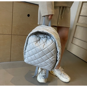 Detail eines hellgrauen gesteppten Rucksacks mit Rautenmuster und blauem Trageriemen