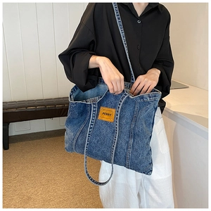 Detailed shot of dark blue denim tote bag featuring a brown leather Penny label on the front