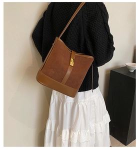 Detail view of brown faux suede bucket bag with gold lock hardware on a model