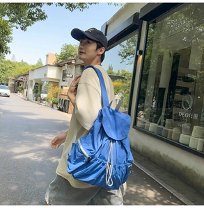 Detail of Klein blue nylon backpack with flap and drawstring closure in outdoor setting