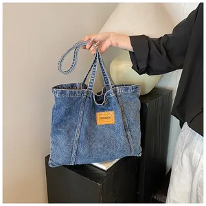 Close-up of blue denim tote bag featuring a brown leather PENNY tag and durable stitching