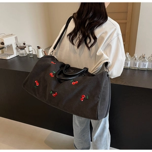 Detail of black canvas tote bag with red cherry embroidery and leather handle on shoulder