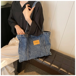 Detailed close-up of dark blue denim tote bag featuring a brown leather PENNY logo patch
