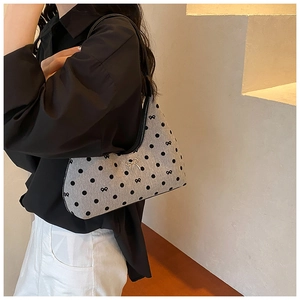 Dettaglio di una borsa a spalla a pois con fiocco metallico indossata dal modello