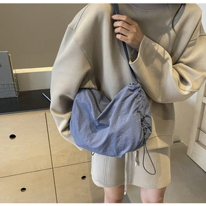 Detail of blue nylon cloud bag with drawstring pleats and side zipper on a model