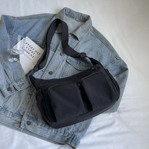 Black nylon crossbody messenger bag with zip pockets on a casual denim jacket
