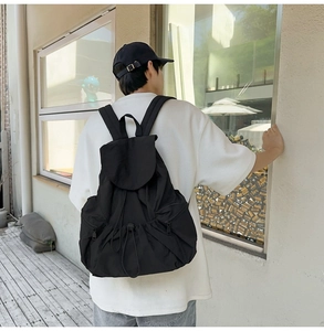 Rear view of a black nylon drawstring backpack worn by a model in an urban setting