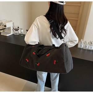 Detailed view of black canvas crossbody bag with red cherry embroidery and strap