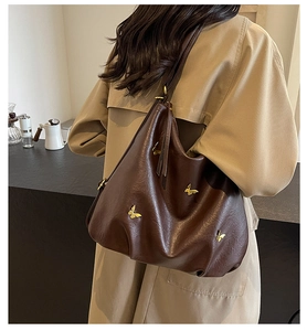 Detail of dark brown faux leather hobo bag with gold butterfly charms worn by model