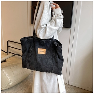 Lifestyle shot of large denim tote bag with brown leather tag worn by a model