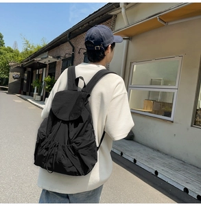 Minimalist black nylon backpack with drawstring closure worn by a model in city street