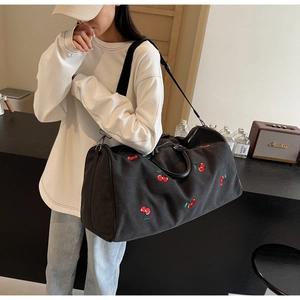 Detail of black canvas tote bag with cherry embroidery showing texture and wide strap