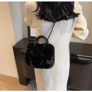 Detail of black faux fur handbag with woven handle worn by model in light dress