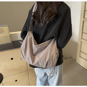 Detail of a large capacity brown nylon dumpling crossbody bag worn by a model in a room