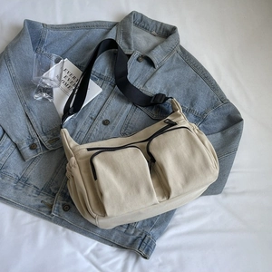 Beige canvas crossbody bag with double front zip pockets and wide black adjustable strap