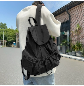 Side view of black nylon backpack with drawstring closure worn by male model outdoors