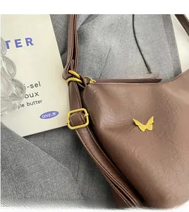 Detail of retro brown PU leather bag featuring a gold butterfly logo and adjustable strap