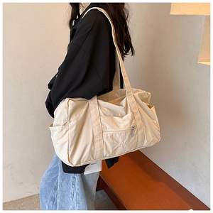 Close-up of beige nylon shoulder bag showing VELLA embroidery and side pocket detail