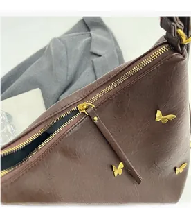 Detail of smooth zipper closure and gold butterfly ornament on brown PU leather bag