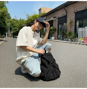 Outdoor street shot of a black nylon drawstring backpack worn by a model in casual attire
