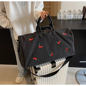 Detail shot of black fabric travel bag with red cherry embroidery on a white suitcase