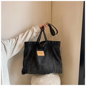 Macro detail of the black denim tote bag featuring the PENNY leather patch and shoulder strap