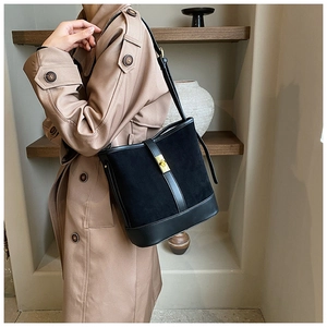Detail of black suede bucket bag with gold metal buckle worn with a beige trench coat