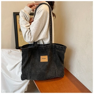 Close-up of a washed denim tote bag with a brown leather label and the text PENNY