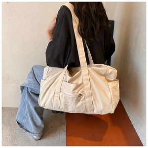 Detail of a beige nylon shoulder bag with zipper pockets and wide strap for daily commute