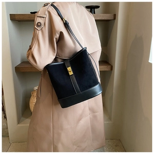 Detail of black faux suede bucket bag with gold clasp shown on a beige trench coat