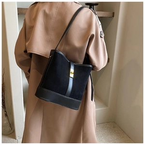 Detail view of black faux suede bucket bag with gold clasp shown on a model