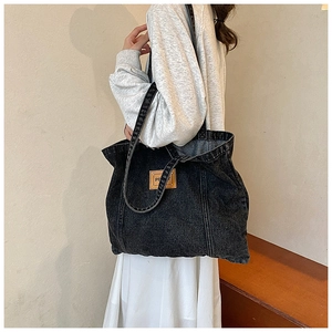 Detail view of large denim tote bag with leather logo patch worn on shoulder by model