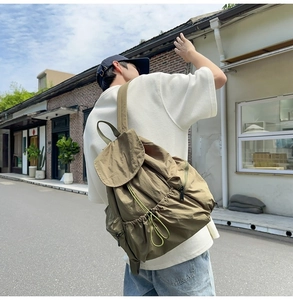 Olive green nylon backpack with drawstring closure and large flap shown in an outdoor setting