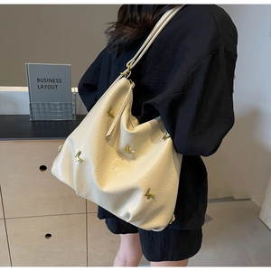 Chic cream PU tote bag with 3D golden butterfly accents worn by a model in a minimalist setting