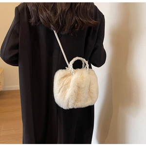 Detail view of cream plush crossbody bag featuring braided handle on a black coat