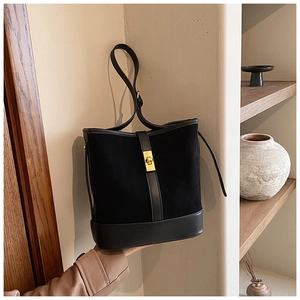 Detail of black suede bucket bag with gold clasp and adjustable strap in hand