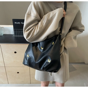 Detail of black PU leather shoulder bag featuring exquisite gold butterfly metal accents