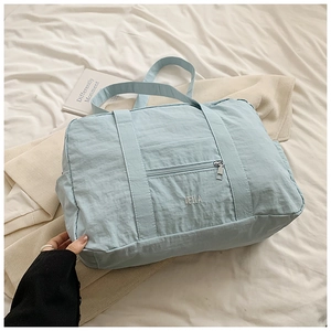 Light blue nylon travel tote bag with double handles and front zipper pocket detail