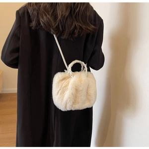 Close-up of plush off-white faux fur crossbody bag with white woven handle on dark coat