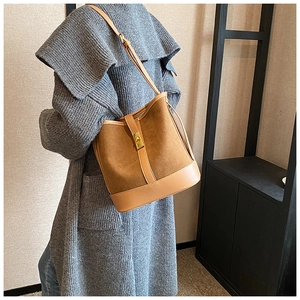 Close-up of brown suede bucket bag featuring golden buckle and slim leather strap